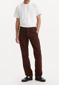 Camiseta blanca de algodón combinada con pantalones de pana marrón, con un corte recto y una textura sutil. Mocasines negros completan el conjunto.