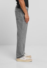 Jeans in denim grigio con vestibilità dritta, dotati di tasca posteriore e passanti per cintura, indossati con sneaker beige e bianche.