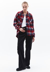Rood en marineblauw geruite flanellen overhemd met twee borstzakken, gedragen over een wit tanktop, gecombineerd met zwarte cargo broeken en zwarte laarzen.