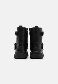 Bottines en cuir noir avec une texture lisse, des zips sur les côtés et des accents en boucle métallique. Semelles en caoutchouc épaisses avec un motif pour une meilleure adhérence.