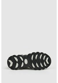 Suela de zapato deportivo negro que presenta una superficie texturizada con un patrón hexagonal y acentos blancos; diseño robusto para tracción.