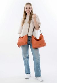 Zwei orangefarbene Lederhandtaschen, die ausgestellt sind, mit einer glatten Textur, weichen Form und braunen Trägern. Eine Tasche ist größer und hat einen oberen Reißverschluss.