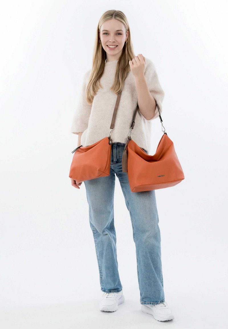 Zwei orangefarbene Lederhandtaschen, die ausgestellt sind, mit einer glatten Textur, weichen Form und braunen Trägern. Eine Tasche ist größer und hat einen oberen Reißverschluss.