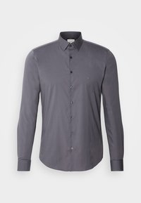Camisa gris de manga larga hecha de una tela suave, con cuello abotonado, botones negros y un logo sutil en el pecho.