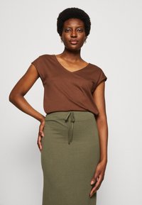 Brown, short-sleeve V-neck top paired with a long, olive green skirt featuring a drawstring waistband, made of soft, lightweight fabric.