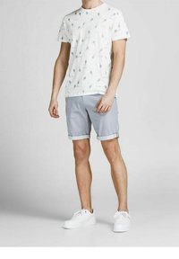 Bílý bavlněný tričko s modrým listovým potiskem, nošené s šedými šortkami s ohrnutými manžetami. Doplňuje bílé tenisky. Minimalistický design.