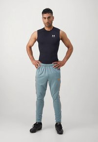 Svart ärmlös sporttopp med vitt logo, kombinerad med ljusblå träningsbyxor med orange sidostripes och bekväm passform. Svarta skor.