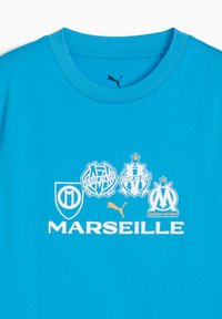 Ryškiai mėlyna marškinėliai su Marseilio futbolo klubo logotipais ir Puma logotipu, po kuriais baltai atspausdinta "MARSEILLE".