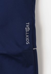Navy blue children’s pants with a smooth texture, featuring a silver "TROLLKIDS" logo and stitching accents.