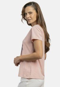 Camiseta de algodón rosa claro con mangas cortas, que presenta un diseño gráfico colorido en el frontal. La tela parece suave y tiene un corte relajado.