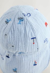 Gorra de algodón azul claro con bordado que presenta motivos marinos como peces, veleros y cangrejos. Tela suave y texturizada con un ajuste relajado.