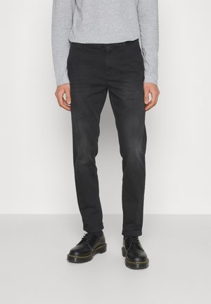 Jean slim noir en denim de coton, avec un design classique à cinq poches et une légère décoloration, associés à des chaussures en cuir noir.