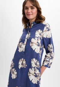 Blaues Leinenkleid mit floralem Muster in Creme und Braun, mit Knopfleiste und Dreiviertelärmel.