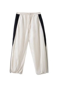 Pantalon blanc ample avec taille et poignets élastiques, avec des panneaux latéraux noirs allant de la taille à l'ourlet.