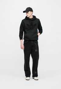 Felpa nera con logo testurizzato, abbinata a jeans neri con dettagli strappati e borchie. Sneakers bianche completano il look.