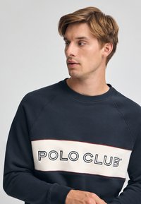 Felpa navy con una striscia crema sul petto che recita "POLO CLUB" in nero, con maniche raglan e design a collo rotondo.