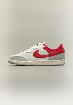 Baskets blanches avec bout gris, talon rouge et logo Swoosh, lacets blancs et doublure intérieure rouge matelassée sur fond neutre.