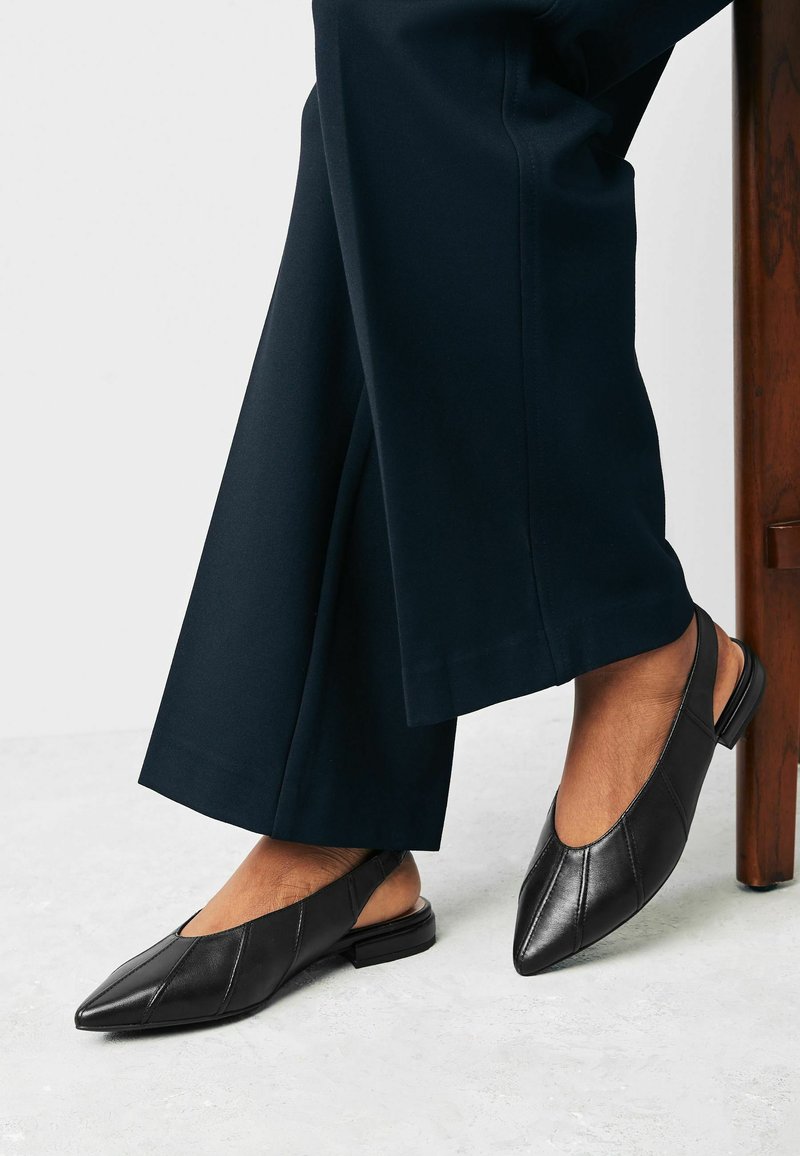 Fekete slingback cipők hegyes orral, puha bőr anyagból, varrott részletekkel és alacsony blokk sarkú, sötét nadrággal párosítva.