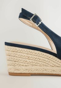 Navyblauwe suède sleehak sandaal met enkelbandje, zilveren gesp en gevlochten jute plateauzool.