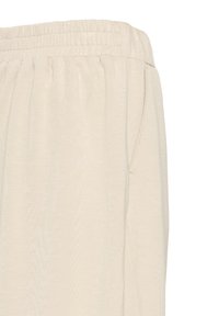 Pantaloni della tuta color beige chiaro con vita elastica, tasche laterali e una consistenza morbida, caratterizzati da un design ampio e rilassato.