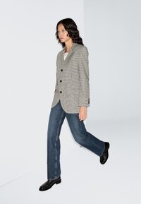 Grijze geruite blazer met een reverskraag en drie knopen, gecombineerd met blauwe recht gesneden jeans en zwarte leren enkellaarzen.