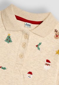 Beige polokošile s vyšitými vánočními motivy: vánoční stromy, Santa Claus, sobi a cesmína. Obsahuje knoflíkovou légu a červenou podšívku límce.