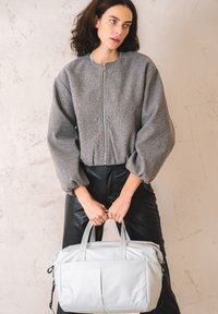 Giacca zip grigia con maniche oversized e gonfie, abbinata a pantaloni neri in ecopelle. Borsa grigia chiara con manici doppi.