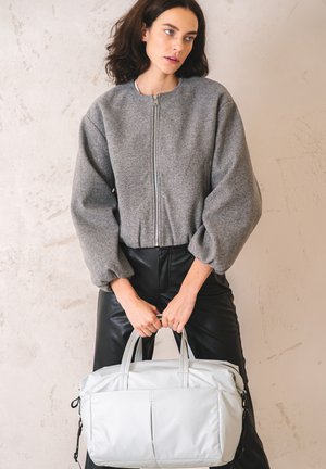 Giacca zip grigia con maniche oversized e gonfie, abbinata a pantaloni neri in ecopelle. Borsa grigia chiara con manici doppi.