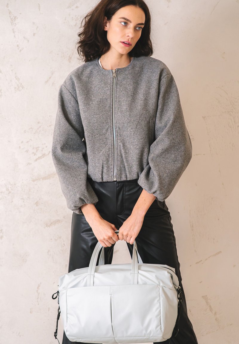 Giacca zip grigia con maniche oversized e gonfie, abbinata a pantaloni neri in ecopelle. Borsa grigia chiara con manici doppi.