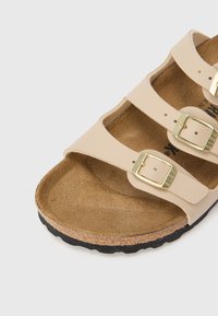 Μπεζ σανδάλι με τρεις ρυθμιζόμενους ιμάντες, χρυσές αγκράφες, ανατομικό πάτο από φελλό και μαύρη ελαστική σόλα.  Ομαλή υφή και μίνιμαλ σχεδιασμός.