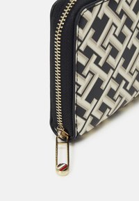 Portafoglio con zip in nero e crema. Presenta un motivo geometrico, hardware oro e un anello laterale con un accento multicolore.