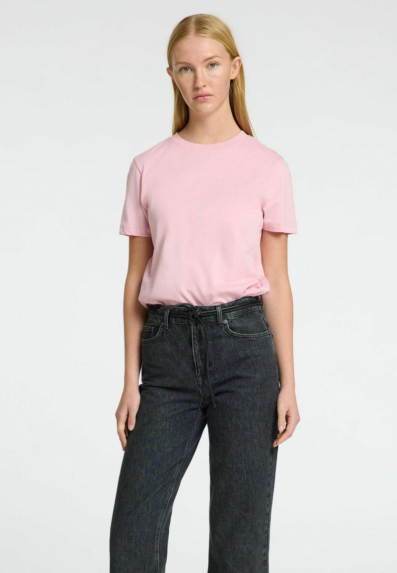 Camiseta de manga corta rosa de algodón, combinada con jeans de mezclilla oscura de talle alto; cuenta con un corte relajado y un diseño sencillo.