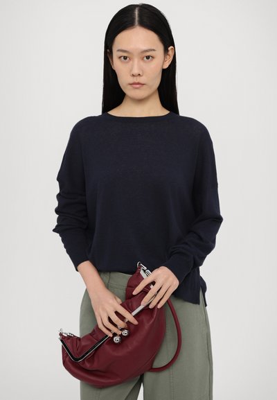 Jūras flotes krāsas adīts džemperis ar garām piedurknēm un ribotām aprocēm, apvienots ar bordo ādas somu ar sudraba detaļām un teksturētu apdari.