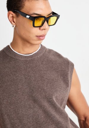 Black rectangular sunglasses with yellow lenses, worn with a brown sleeveless sweater. Accented with a white bear logo on the frame.