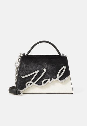 Borsa in bianco e nero con superficie testurizzata simile alla pelliccia, caratterizzata da un logo "Karl" in argento in corsivo. Include un manico superiore e una tracolla a catena.