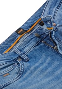 Riflové džíny světle modré barvy, s klasickým designem pěti kapes, kovovým zipem, zapínáním na knoflík a oranžovým vnitřním páskem s logem.