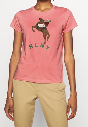 Rosa Baumwoll-T-Shirt mit einem Grafikdesign eines Pferdes und Reiters, darunter die Buchstaben "RLNY" in grün. Mit kurzen Ärmeln und runder Ausschnitt.