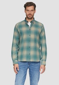 Groene en beige geblokte overhemd met een kraag, lange mouwen en zwarte knopen, gecombineerd met blauwe denim jeans.