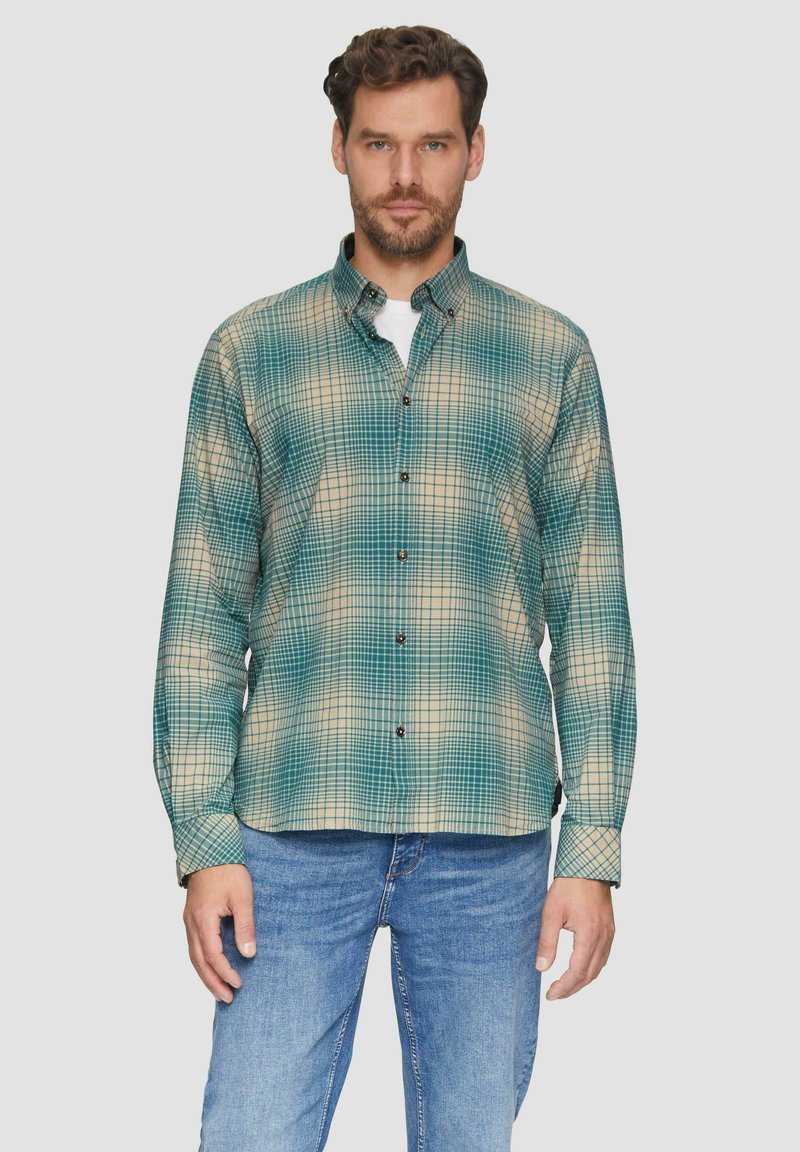 Groene en beige geblokte overhemd met een kraag, lange mouwen en zwarte knopen, gecombineerd met blauwe denim jeans.