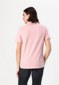 Lichtroze polo shirt met een klassieke kraag en korte mouwen, gemaakt van zacht katoen. De achterkant heeft een eenvoudig ontwerp zonder extra details.