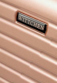 Roze gouden koffer met geribbelde textuur; voorzien van een zwart metalen logo plaquette met de tekst "WITTCHEN" voor branding. Gladde, glanzende afwerking.