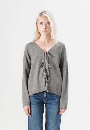 Gray knitted sweater with a deep V-neck, front ties, and wide sleeves; paired with blue jeans; textured fabric, relaxed fit.
