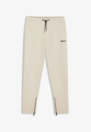 Jasnobeżowe spodnie dresowe wykonane z miękkiego materiału, z elastycznym paskiem w talii, sznurkiem do wiązania, bocznymi kieszeniami oraz zamkami na mankietach. Widoczny logo "BOSS".