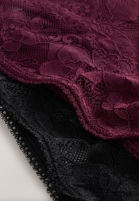 Sötétvörös és fekete virágos csipkés anyag rétegezve, finom részletekkel és hullámos szegélyekkel egy sima felületen.