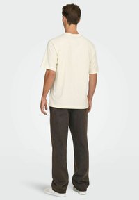 Kremfarvet bomulds-T-shirt med korte ærmer og løs pasform. Kombineret med mørkebrune, løstsiddende bukser og hvide sneakers.