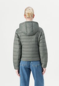 Polstret jakke i dempet grønn med hette, med horisontale sømmer og cropped snitt, parret med høyt liv blå jeans.
