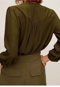 Blusa verde oliva con maniche a sbuffo e design della schiena plissettata, abbinata a pantaloni verde oliva a vita alta con tasche posteriori.