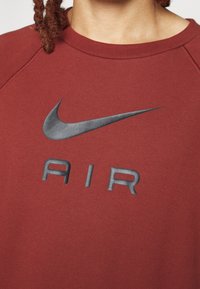 Personne portant un sweat-shirt bordeaux avec un logo Nike noir et le mot "AIR" imprimé sur la poitrine.