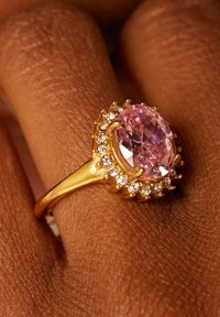 Gold ring featuring an oval pink gemstone surrounded by small clear stones, set in a textured band with a claw-like design.