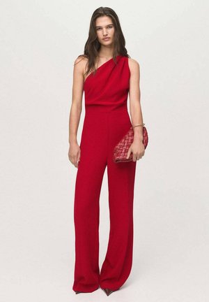 Red one-shoulder jumpsuit with wide-leg design; smooth texture; paired with a quilted red clutch and gold bangle bracelet.